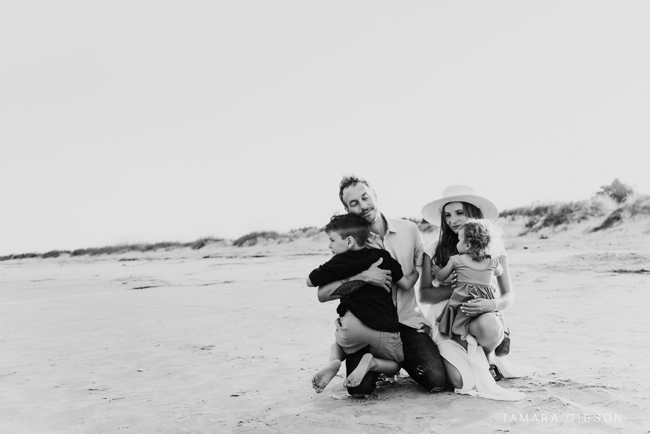 Hallen family of four embrace on the beach.